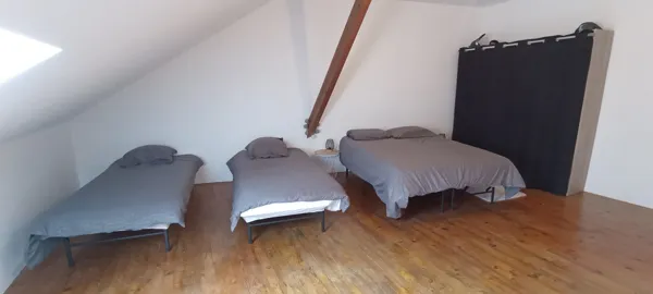 Chambre spacieuse sous les combles avec un lit double et deux lits simples, idéale pour les familles ou groupes.