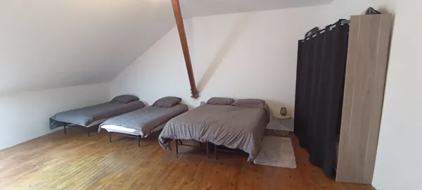 Chambre sous combles avec un lit double et deux lits simples, offrant confort et espace pour plusieurs personnes.