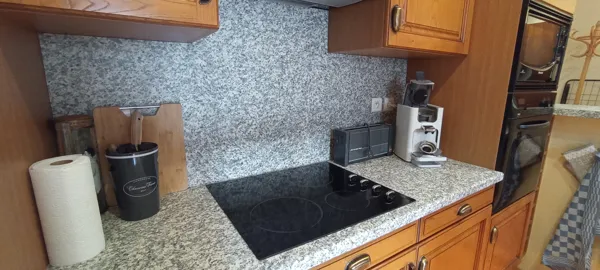 Cuisine équipée avec plan de travail en granit, four, machine à café et accessoires pratiques pour préparer vos repas.