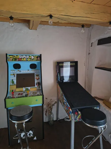 Espace jeux avec borne d’arcade, flipper et jeux de fléchettes, idéal pour des moments de détente en famille à Saisonnée., Maison d’hôtes Saisonnée