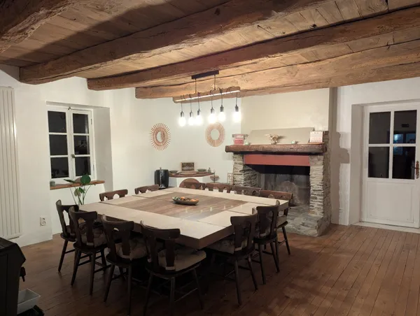 Salle à manger chaleureuse de Saisonnée, avec grande table en bois et cheminée en pierre, idéale pour petit déjeuner et les repas en table d’hôtes., Maison d’hôtes Saisonnée