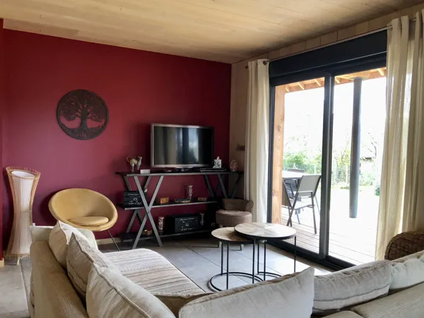 Le salon avec baie vitrée qui donne sur la terrasse couverte et le jardin., 