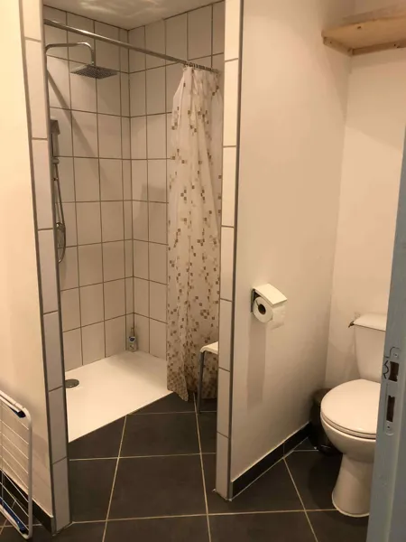Grande douche avec chaise à disposition et wc avec barre d'appui.